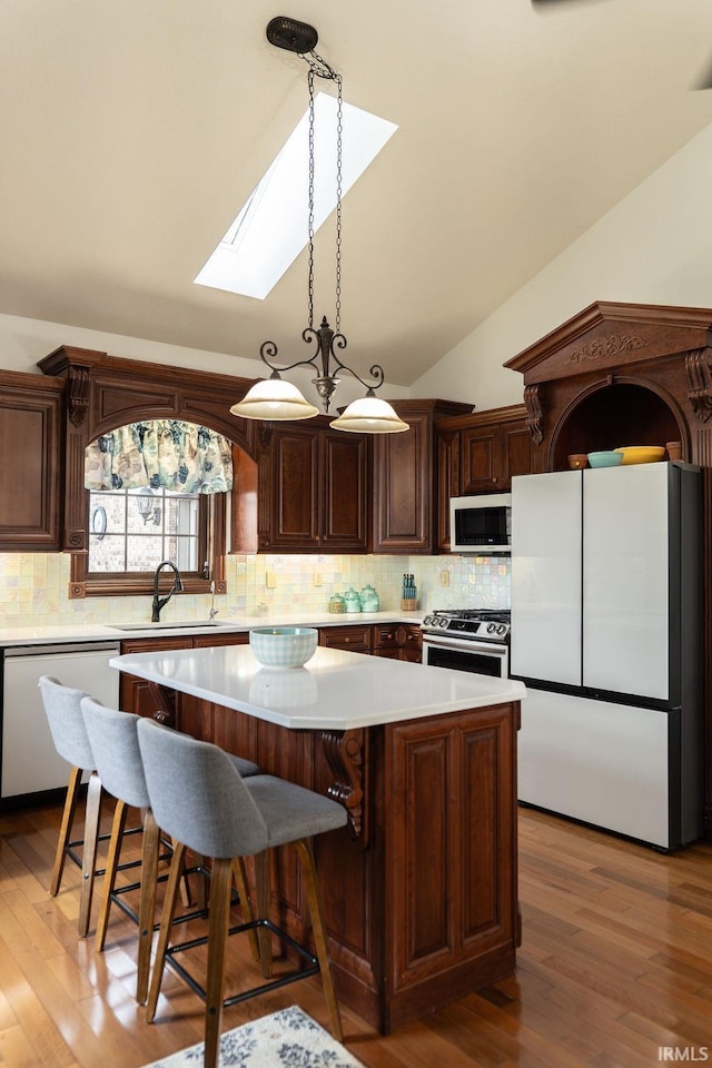 kitchen featuring sink, lofted ceiling with skylight, hardwood / wood-style floors, white appliances, and a kitchen island