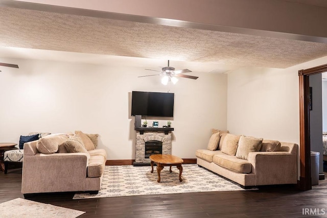 living room with a textured ceiling, ceiling fan, dark hardwood / wood-style flooring, and a fireplace