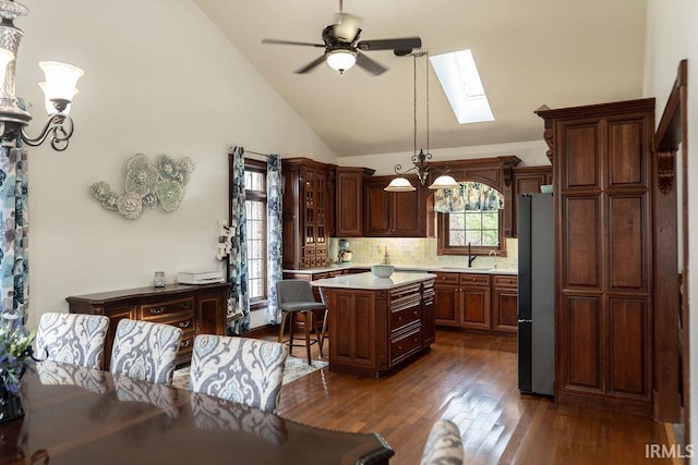 kitchen with high vaulted ceiling, ceiling fan with notable chandelier, a skylight, a kitchen island, and dark hardwood / wood-style flooring