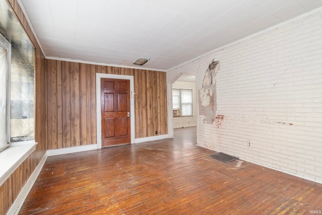 empty room featuring wood-type flooring, wooden walls, and brick wall