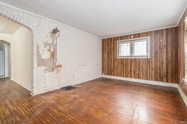 unfurnished room featuring dark hardwood / wood-style flooring, wooden walls, and brick wall