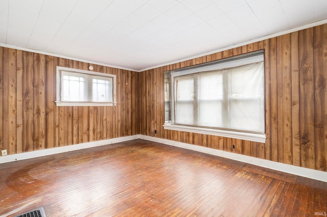 unfurnished room with a wealth of natural light, wooden walls, and wood-type flooring