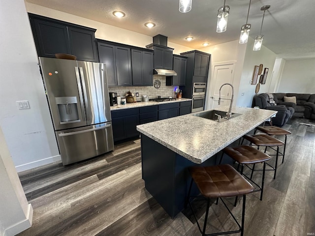 kitchen with a breakfast bar, a kitchen island with sink, hanging light fixtures, sink, and stainless steel appliances