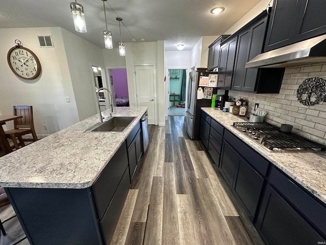 kitchen with appliances with stainless steel finishes, dark hardwood / wood-style flooring, backsplash, sink, and a center island with sink