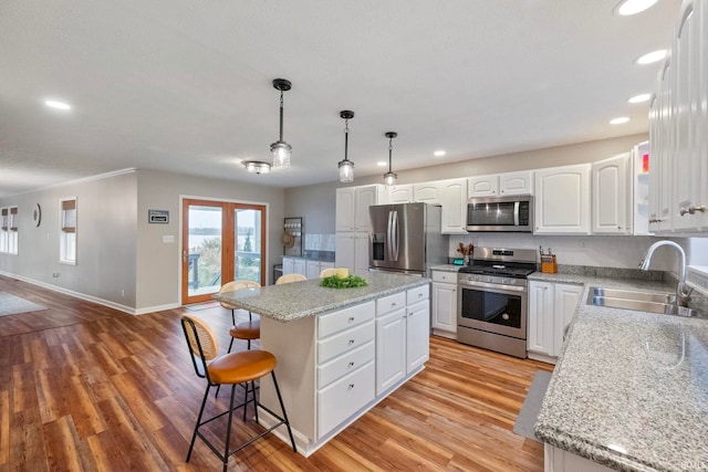 kitchen featuring appliances with stainless steel finishes, sink, white cabinets, a kitchen island, and hanging light fixtures