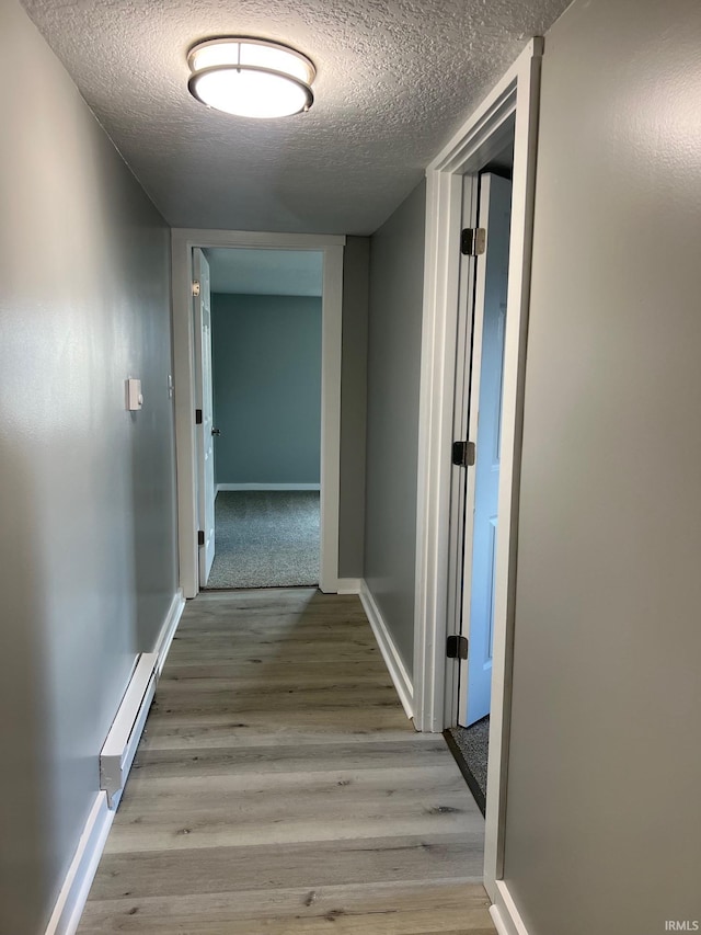 hallway featuring a textured ceiling, a baseboard radiator, and light hardwood / wood-style flooring