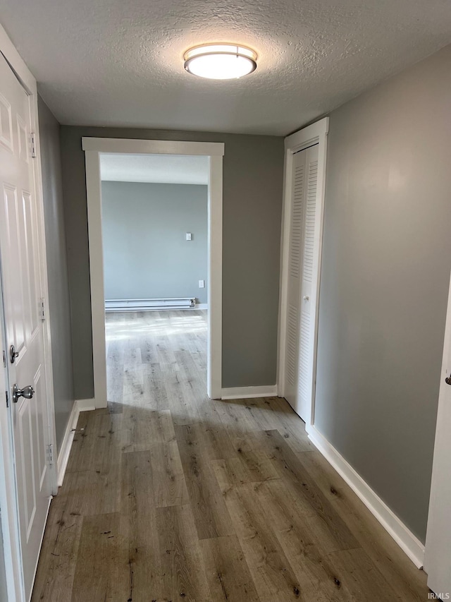 hall with light hardwood / wood-style floors, a textured ceiling, and a baseboard heating unit