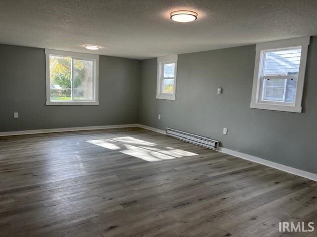 empty room with a wealth of natural light, baseboard heating, and dark wood-type flooring