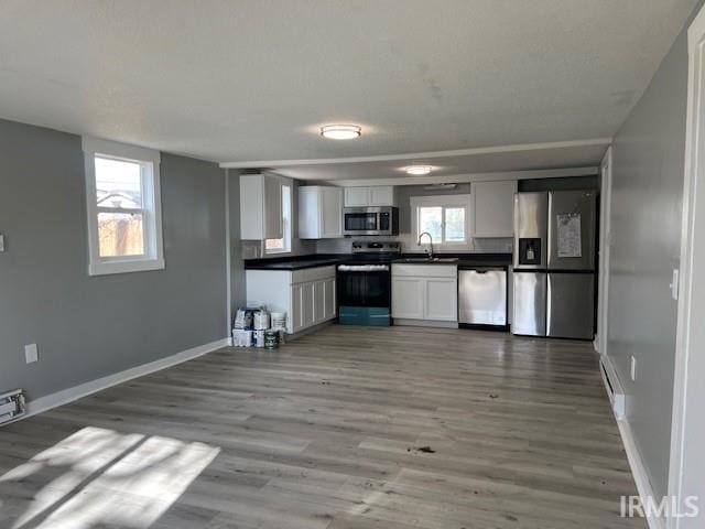 kitchen featuring wood-type flooring, white cabinets, a healthy amount of sunlight, and appliances with stainless steel finishes