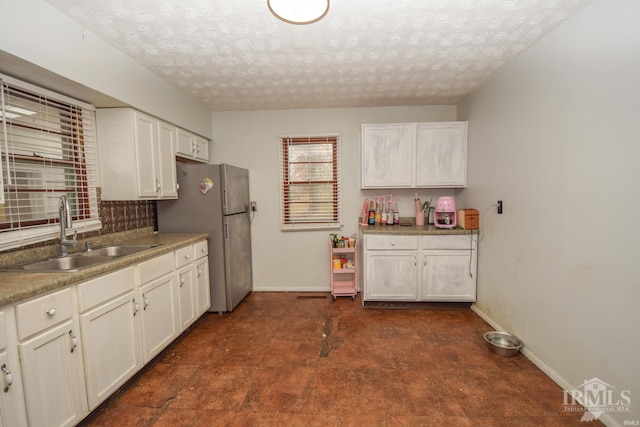 kitchen with a textured ceiling, white cabinetry, sink, and stainless steel refrigerator