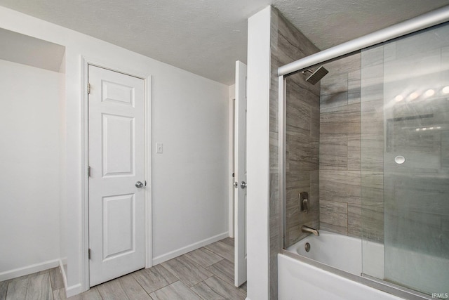 bathroom featuring a textured ceiling and combined bath / shower with glass door