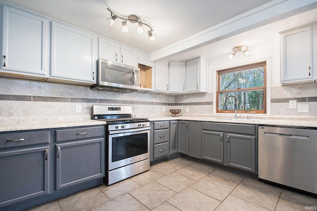 kitchen featuring decorative backsplash, stainless steel appliances, sink, white cabinetry, and light tile patterned flooring