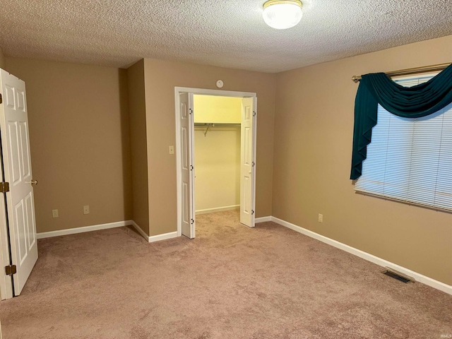 unfurnished bedroom featuring a walk in closet, light carpet, a closet, and a textured ceiling