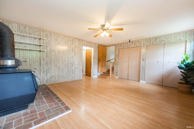 living room featuring a wood stove, ceiling fan, wood walls, hardwood / wood-style floors, and ornamental molding