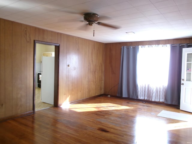 spare room with ceiling fan, wooden walls, and light hardwood / wood-style flooring