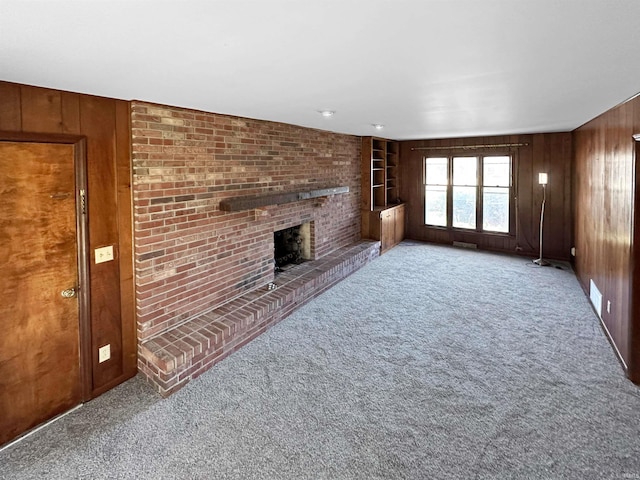 unfurnished living room featuring carpet flooring, a fireplace, and wooden walls