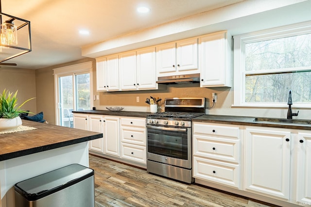 kitchen featuring white cabinets, stainless steel range with gas cooktop, sink, decorative light fixtures, and wood-type flooring