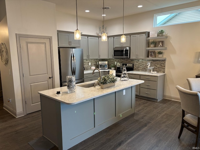 kitchen featuring dark hardwood / wood-style flooring, stainless steel appliances, sink, decorative light fixtures, and an island with sink