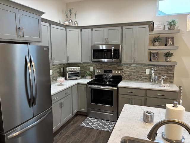 kitchen featuring gray cabinetry, light stone countertops, stainless steel appliances, tasteful backsplash, and dark hardwood / wood-style floors