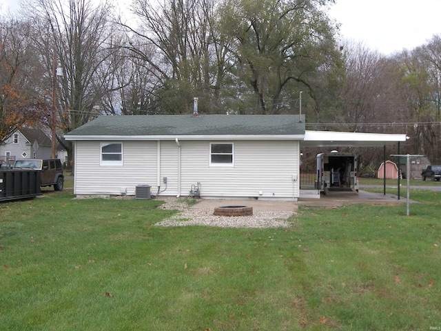 rear view of property featuring a fire pit, a carport, a yard, and central AC