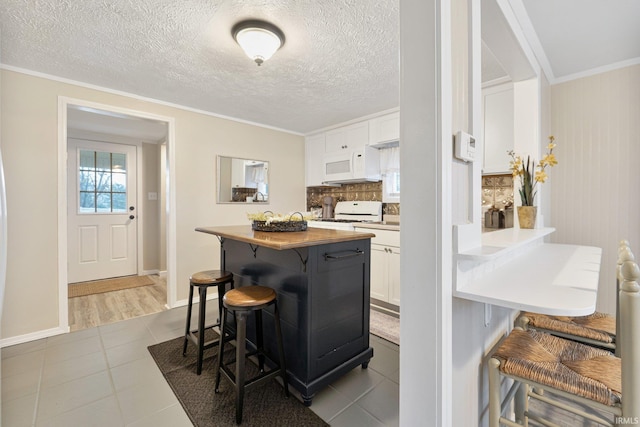 kitchen featuring a breakfast bar, white appliances, tile patterned floors, tasteful backsplash, and white cabinetry