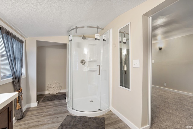 bathroom with vanity, wood-type flooring, vaulted ceiling, a textured ceiling, and a shower with shower door