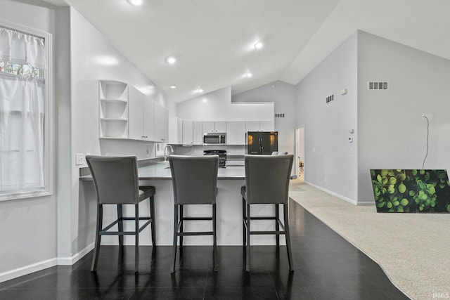 kitchen featuring white cabinetry, high vaulted ceiling, kitchen peninsula, a kitchen bar, and black appliances