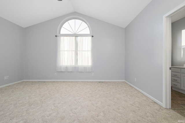 spare room featuring light colored carpet and vaulted ceiling