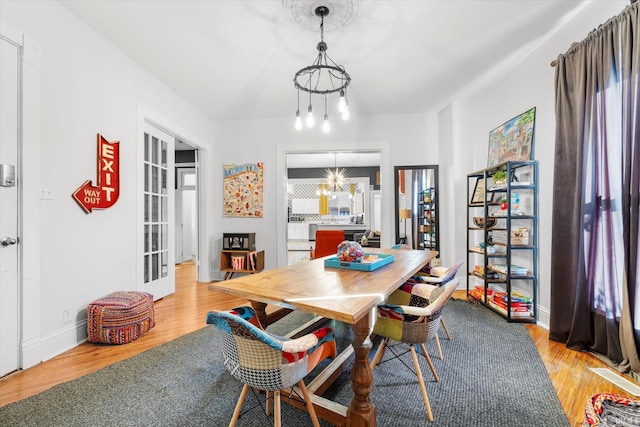 dining area with light wood-type flooring, french doors, and a chandelier