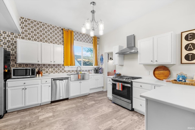 kitchen featuring white cabinetry, sink, stainless steel appliances, and wall chimney range hood