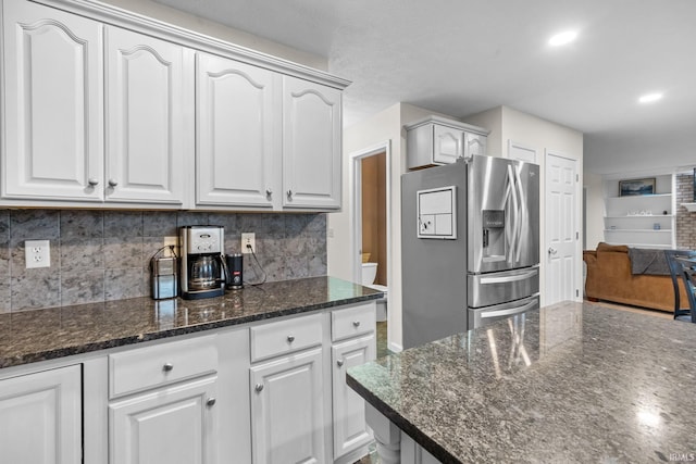 kitchen featuring decorative backsplash, stainless steel fridge, white cabinetry, and dark stone countertops