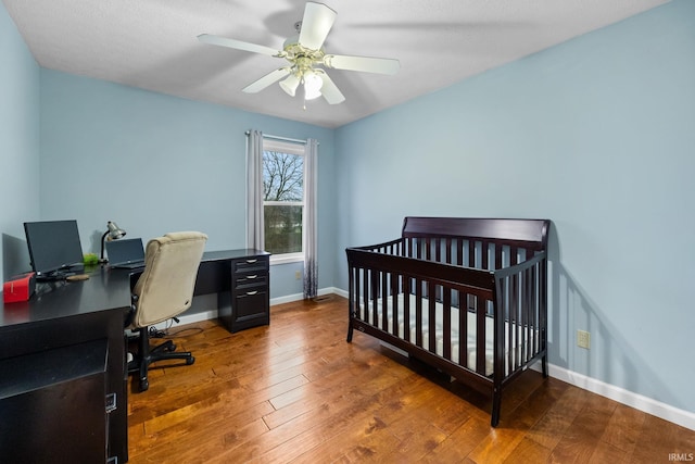 bedroom featuring ceiling fan, dark hardwood / wood-style floors, and a crib