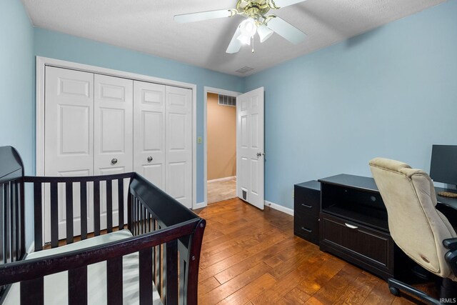 bedroom featuring ceiling fan, dark hardwood / wood-style flooring, a textured ceiling, a closet, and a nursery area