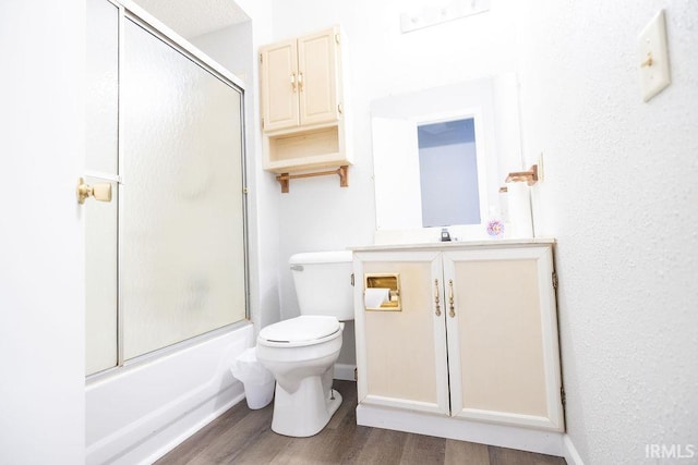 full bathroom with hardwood / wood-style flooring, toilet, combined bath / shower with glass door, and vanity