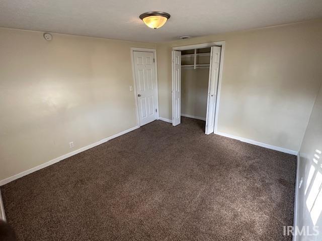 unfurnished bedroom with dark carpet and a closet