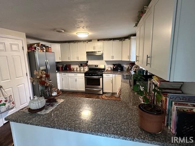 kitchen with kitchen peninsula, appliances with stainless steel finishes, white cabinets, and dark stone countertops