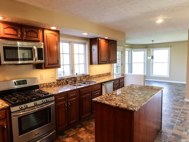 kitchen featuring appliances with stainless steel finishes, a textured ceiling, sink, decorative light fixtures, and a center island