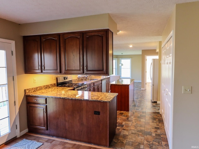 kitchen featuring light stone countertops, sink, stainless steel appliances, kitchen peninsula, and a textured ceiling