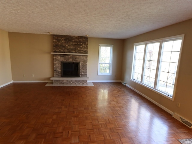 unfurnished living room featuring dark parquet flooring, a textured ceiling, and a brick fireplace