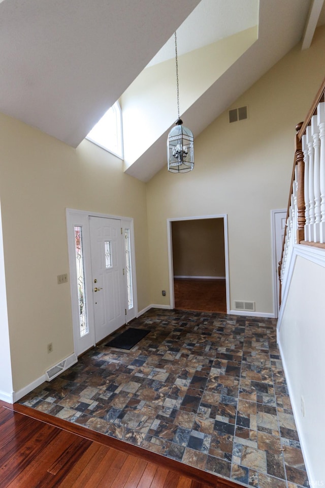 foyer entrance featuring a healthy amount of sunlight, dark wood-type flooring, high vaulted ceiling, and a chandelier