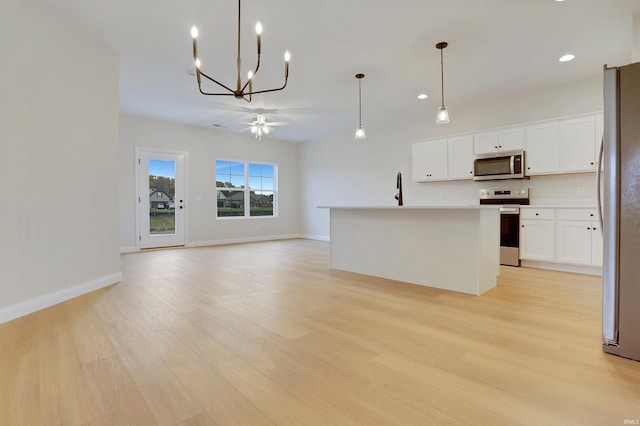 kitchen featuring white cabinetry, hanging light fixtures, light wood-type flooring, appliances with stainless steel finishes, and a kitchen island with sink