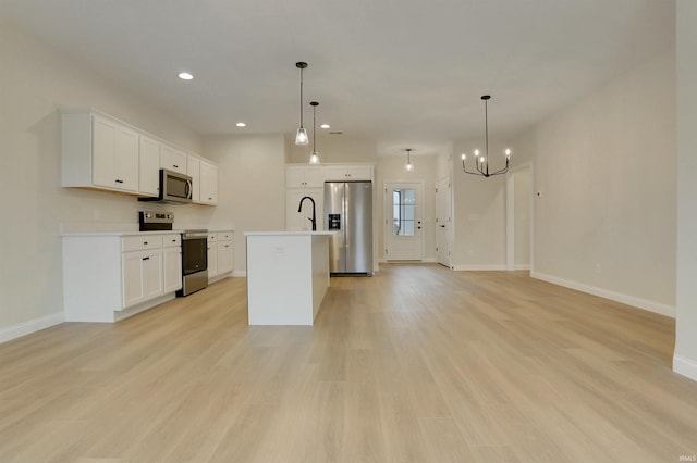 kitchen featuring appliances with stainless steel finishes, decorative light fixtures, an island with sink, and white cabinets