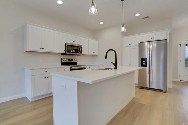 kitchen with stainless steel appliances, sink, a kitchen island with sink, and white cabinets