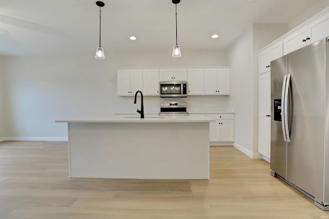 kitchen featuring white cabinetry, stainless steel appliances, decorative light fixtures, and an island with sink