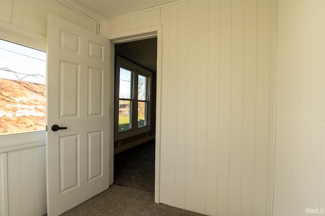 hall with wooden walls and dark colored carpet