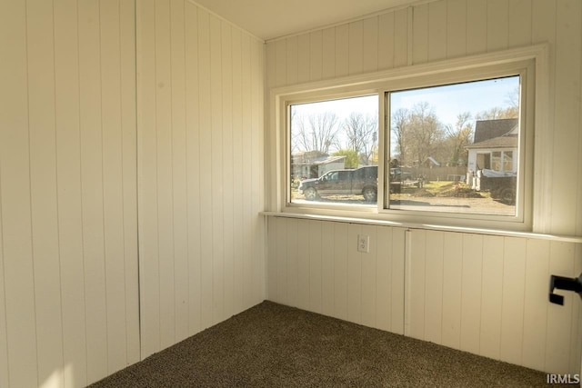 unfurnished room featuring wooden walls and dark carpet