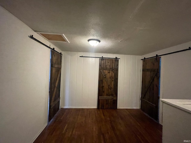 unfurnished bedroom featuring a barn door, dark hardwood / wood-style flooring, and a textured ceiling