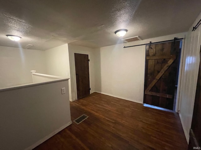 empty room featuring dark hardwood / wood-style floors, a barn door, and a textured ceiling