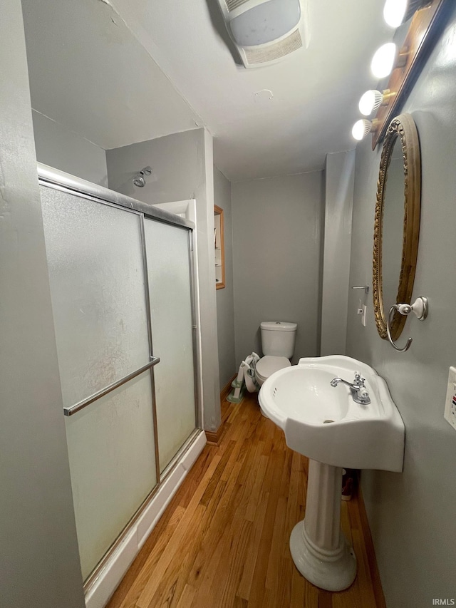 bathroom featuring hardwood / wood-style floors, toilet, a shower with door, and sink