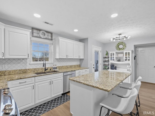 kitchen with sink, light wood-type flooring, appliances with stainless steel finishes, a kitchen island, and white cabinetry